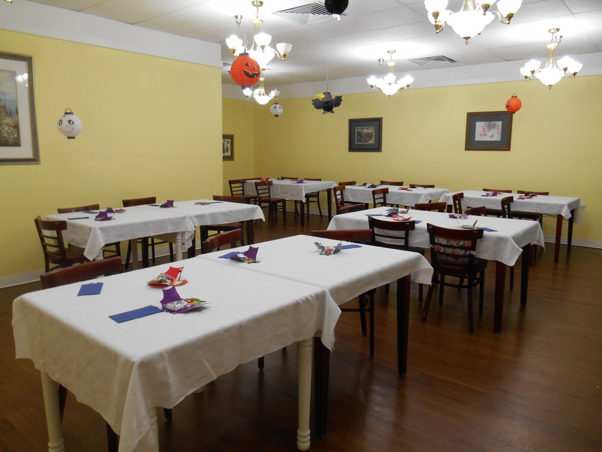 A neatly arranged dining area with tables covered in white tablecloths and chairs around them.