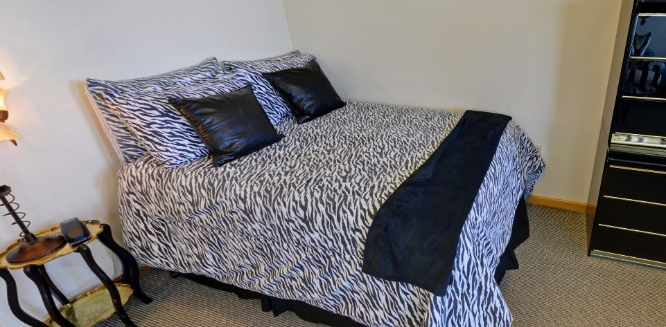 A bed with zebra print bedding and black pillows.