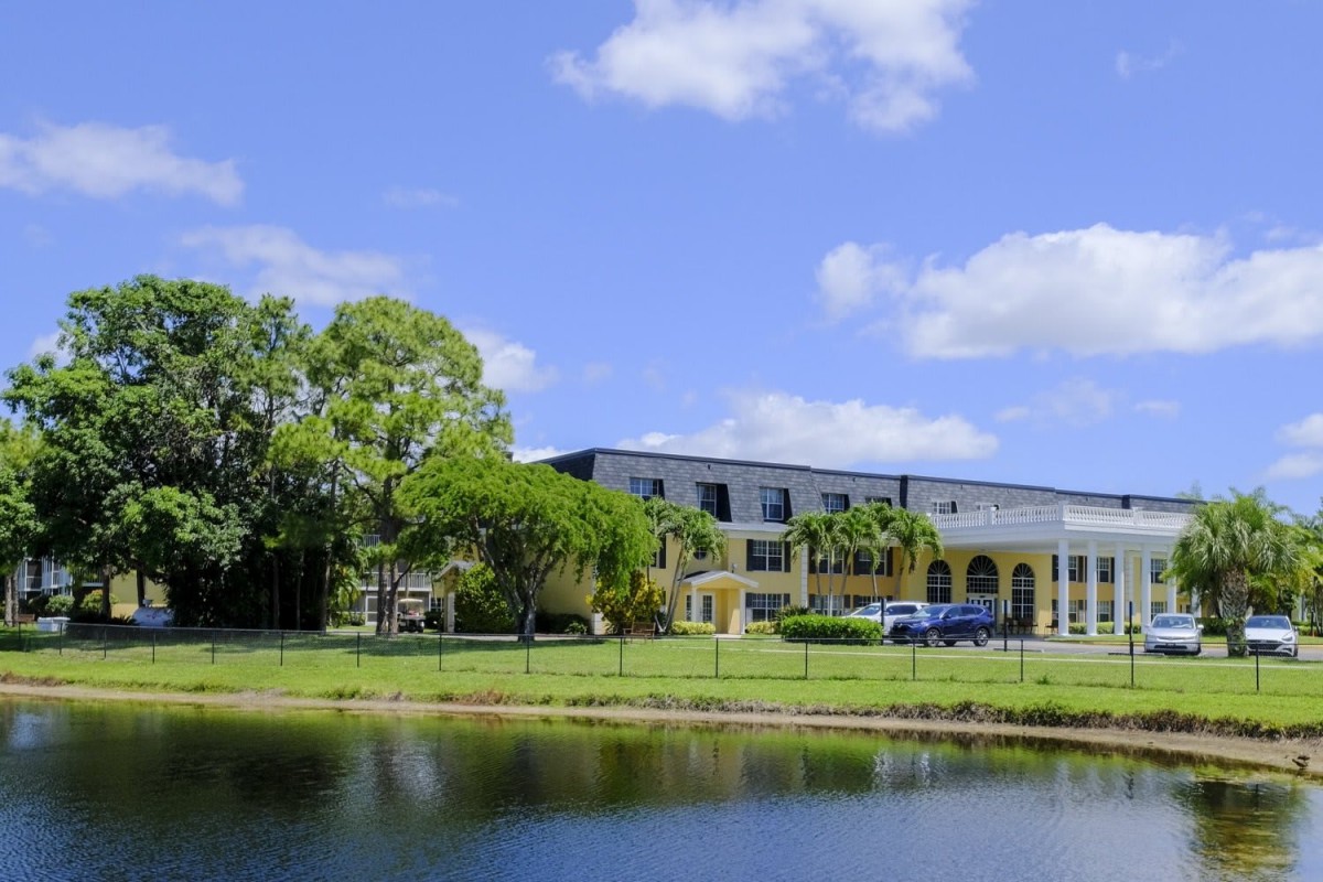 A building by a lake surrounded by trees under a bright blue sky.