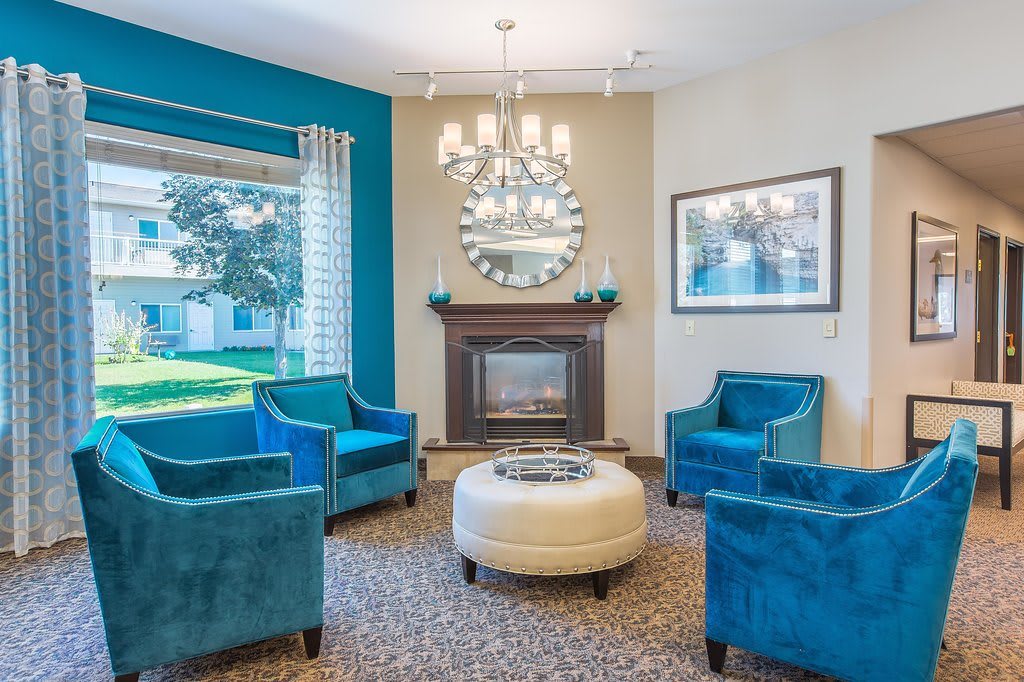 A cozy living room with blue chairs and a fireplace, featuring elegant decor including a mirror and chandelier.