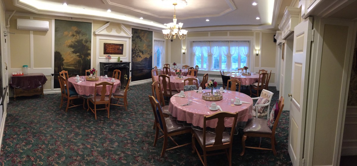 An elegant dining room with round tables, set for a formal event, featuring chandeliers and decorative elements.