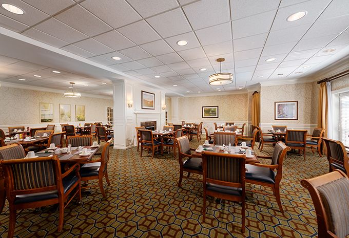 A spacious dining room with neatly arranged tables and chairs, featuring elegant lighting and a patterned carpet.