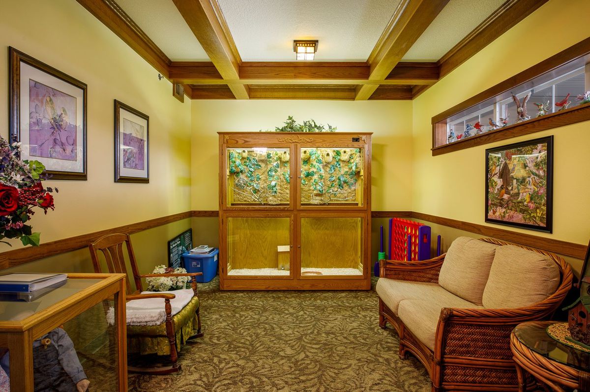A cozy living room with wooden furniture and carpeted flooring, featuring artwork on the walls.
