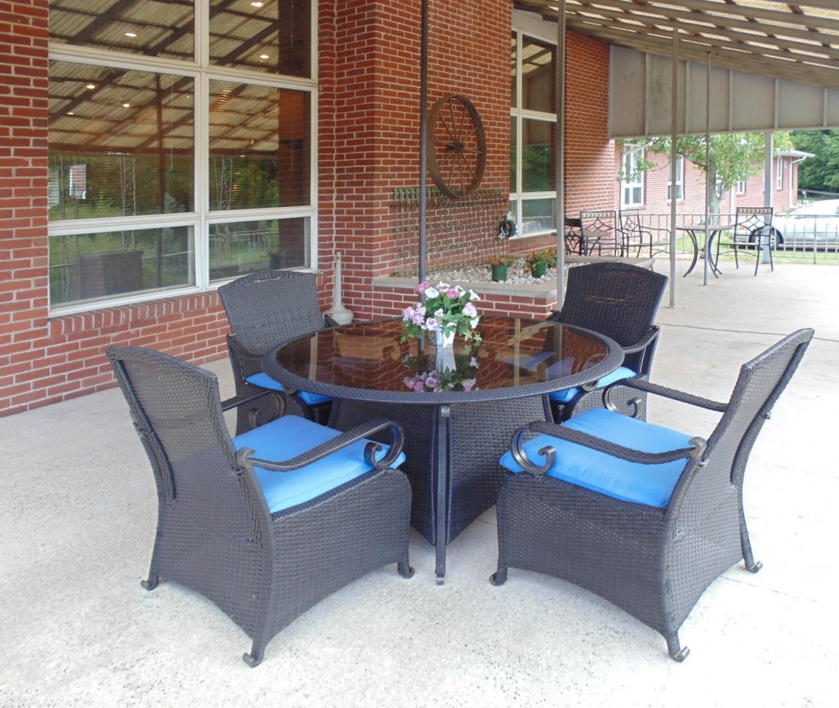 A patio setting with wicker chairs and a glass-top table against a brick wall.