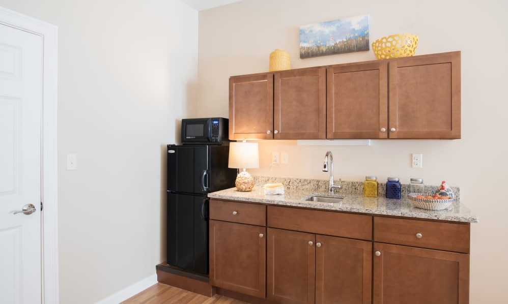 A compact kitchen area with wooden cabinets, a refrigerator, microwave, and decorative elements.