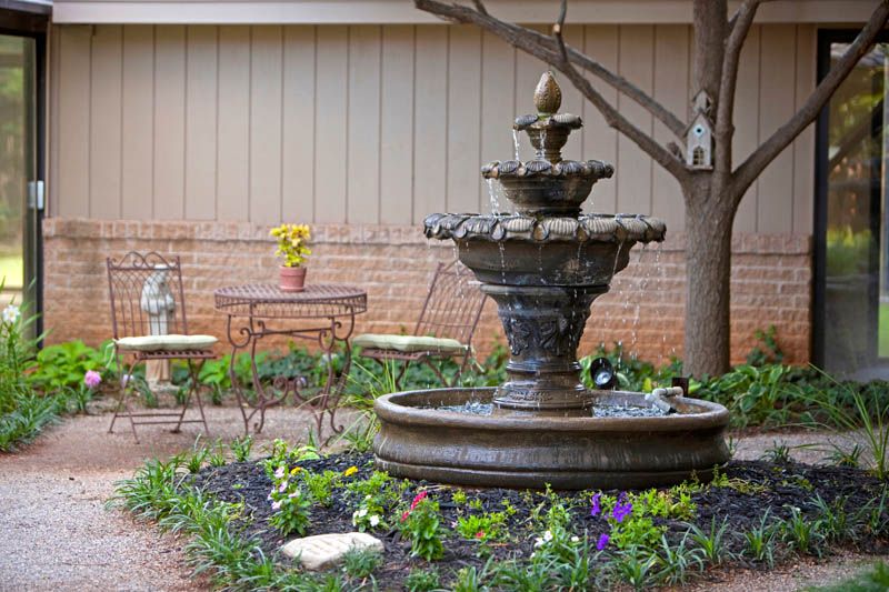 A serene garden patio featuring a decorative fountain surrounded by colorful flowers and outdoor seating.
