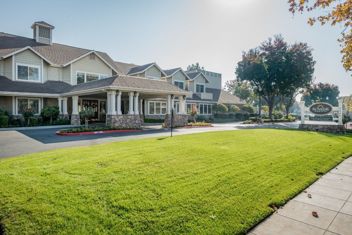 A large suburban house with a green lawn and trees under bright sunlight.