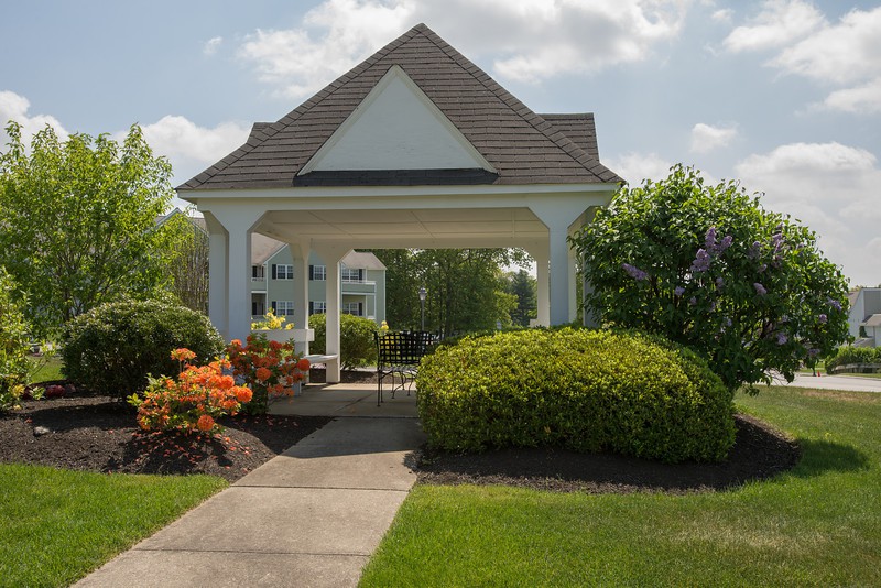 A charming gazebo surrounded by lush landscaping and vibrant flowers on a sunny day.