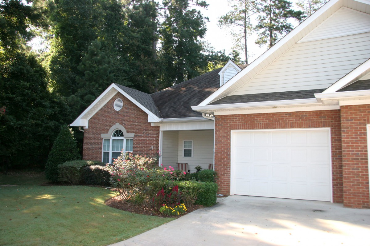 A suburban house with a brick exterior, attached garage, and well-maintained lawn surrounded by trees.