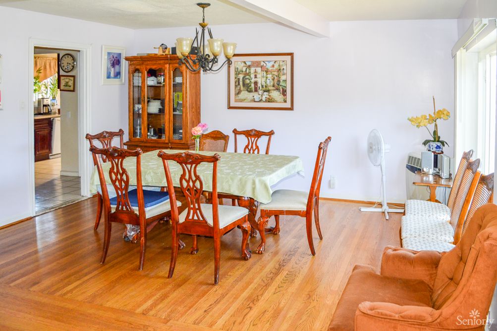 A well-lit dining room with a wooden table and chairs, a glass cabinet, and a chandelier.