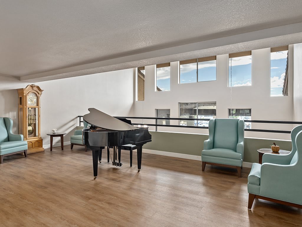 A modern lounge area featuring a grand piano and comfortable seating with ample natural light from large windows.