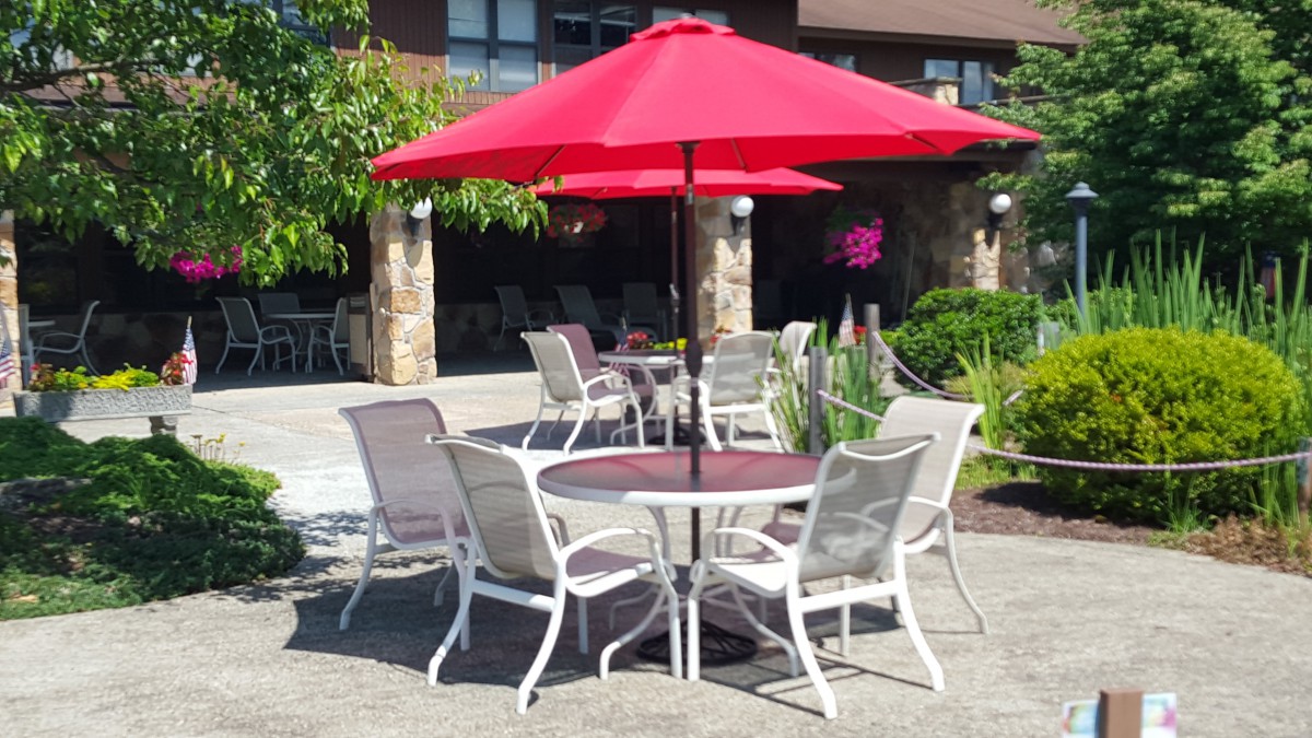 A patio setup with a red umbrella and white chairs around a table.