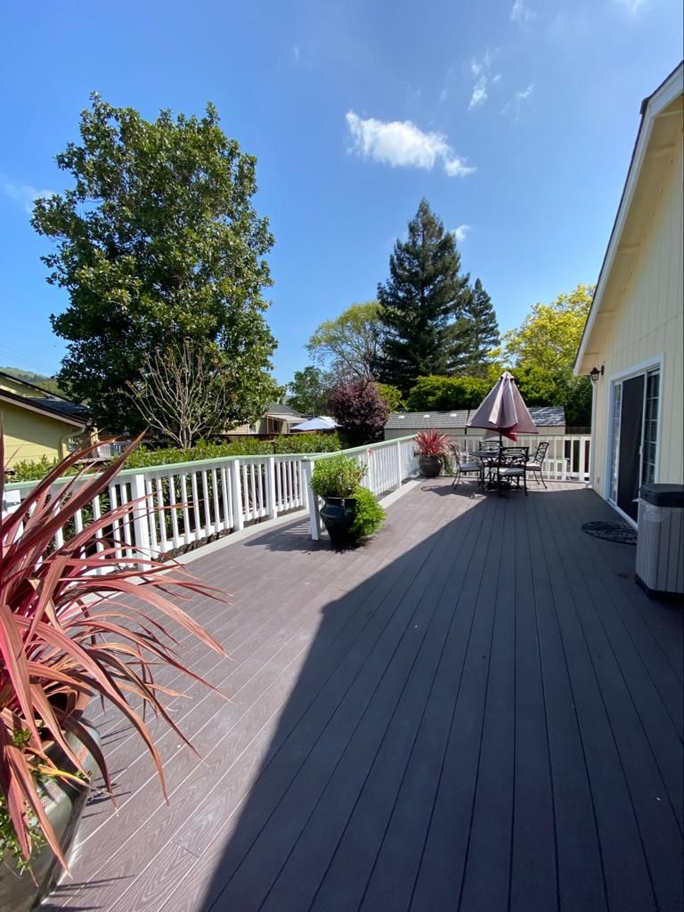 A sunny deck with outdoor furniture, surrounded by trees and potted plants.