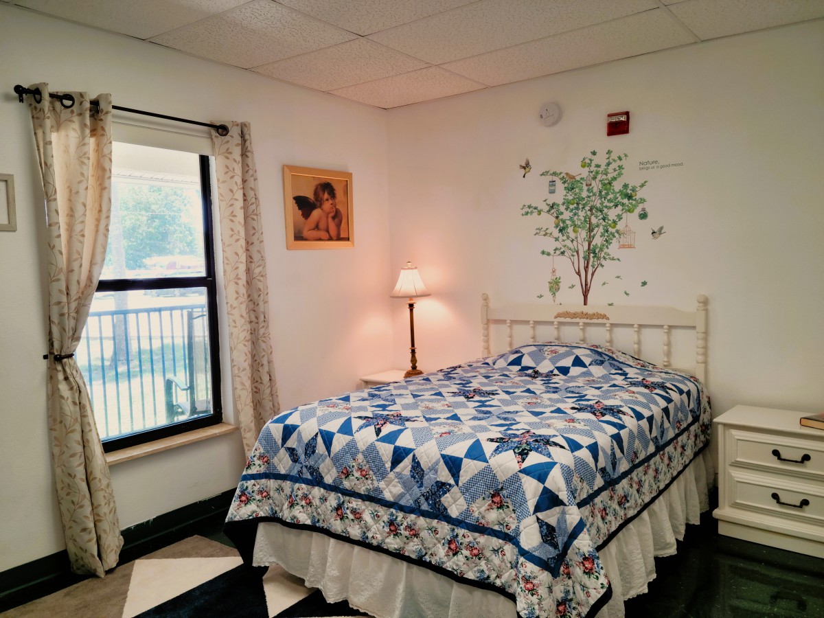 A cozy bedroom with a quilt-covered bed, a lamp, and wall decorations.
