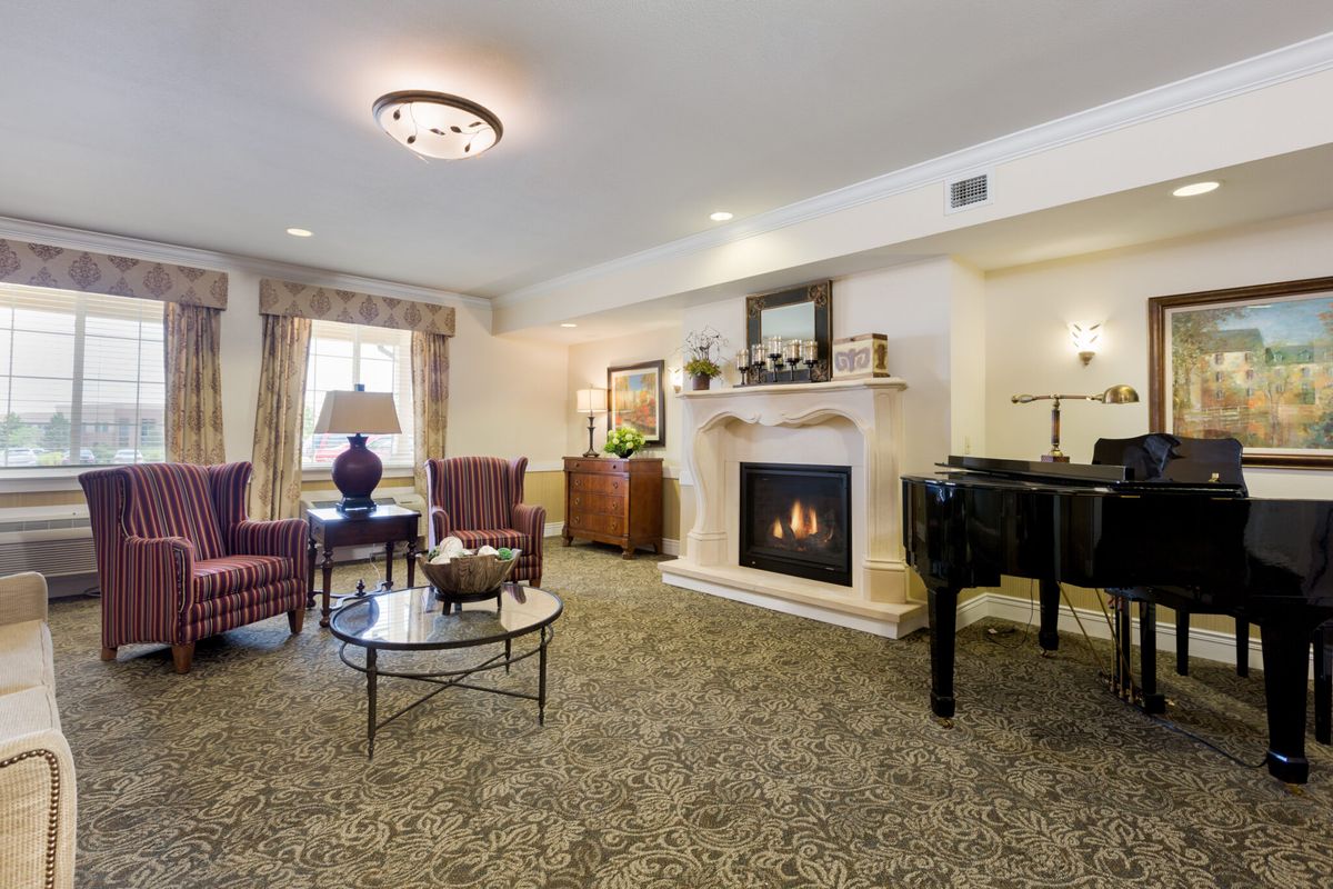 A cozy living room with a fireplace and grand piano, featuring elegant furniture and warm lighting.
