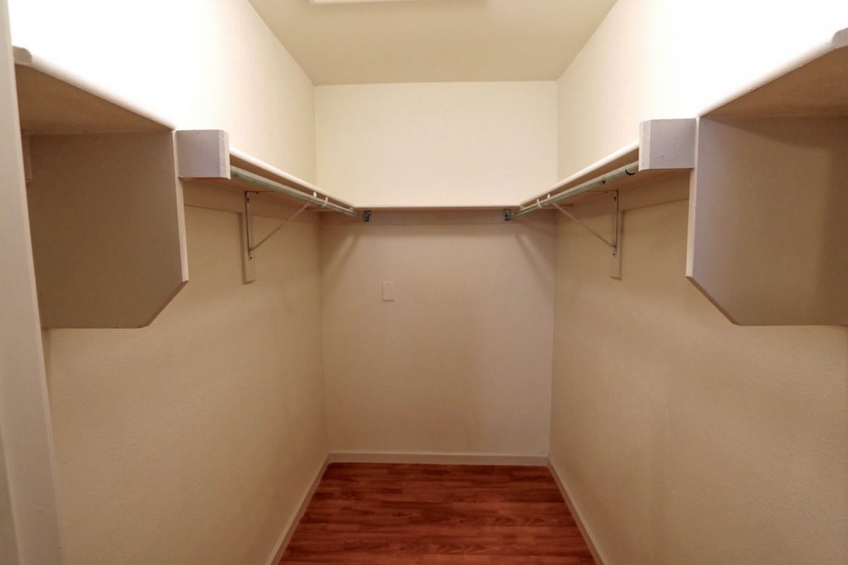 An empty walk-in closet with wooden flooring and hanging rods.