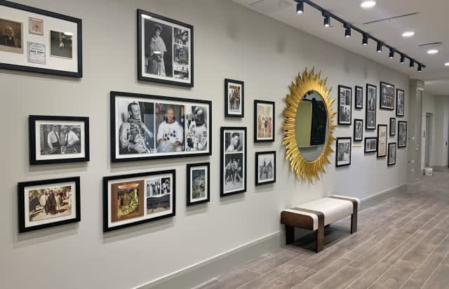 A stylish gallery wall featuring framed black and white photographs, complemented by a decorative sunburst mirror and a bench.