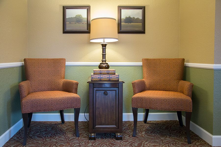 A cozy living room setup featuring two armchairs, a side table with stacked books, and a lamp.