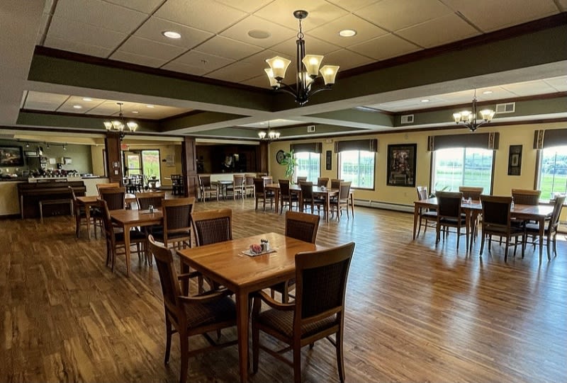 A spacious dining area with wooden tables and chairs, featuring a chandelier and large windows.