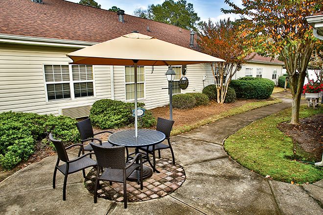A cozy outdoor patio with a table, chairs, and an umbrella situated in a well-maintained garden area beside a house.