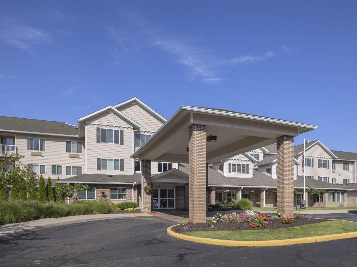 A modern residential building with a covered entrance and well-maintained landscaping under a clear blue sky.