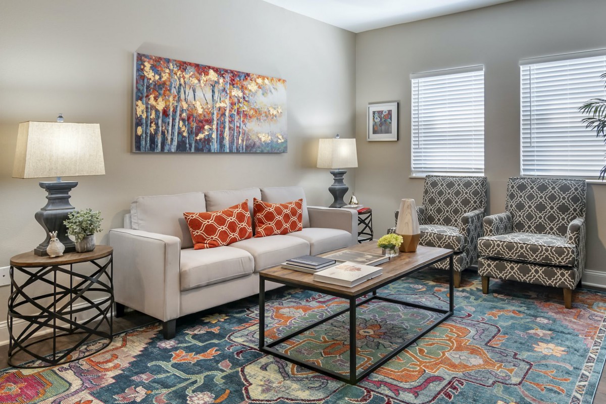 A cozy and stylish living room with a comfortable sofa, colorful pillows, a wood and metal coffee table, abstract artwork, and modern lighting.