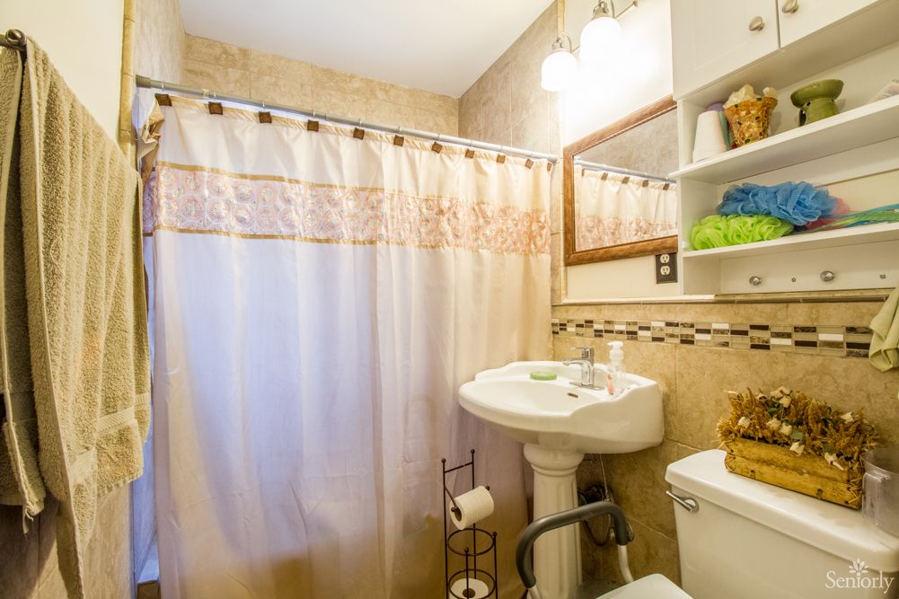 A cozy bathroom with a shower curtain, pedestal sink, and wall-mounted mirror.