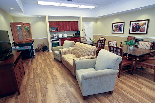 A cozy living room with a couch, chairs, and a dining table, adjacent to a small kitchen area.