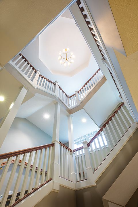 Looking up at a multi-level staircase with white railings and a central chandelier.