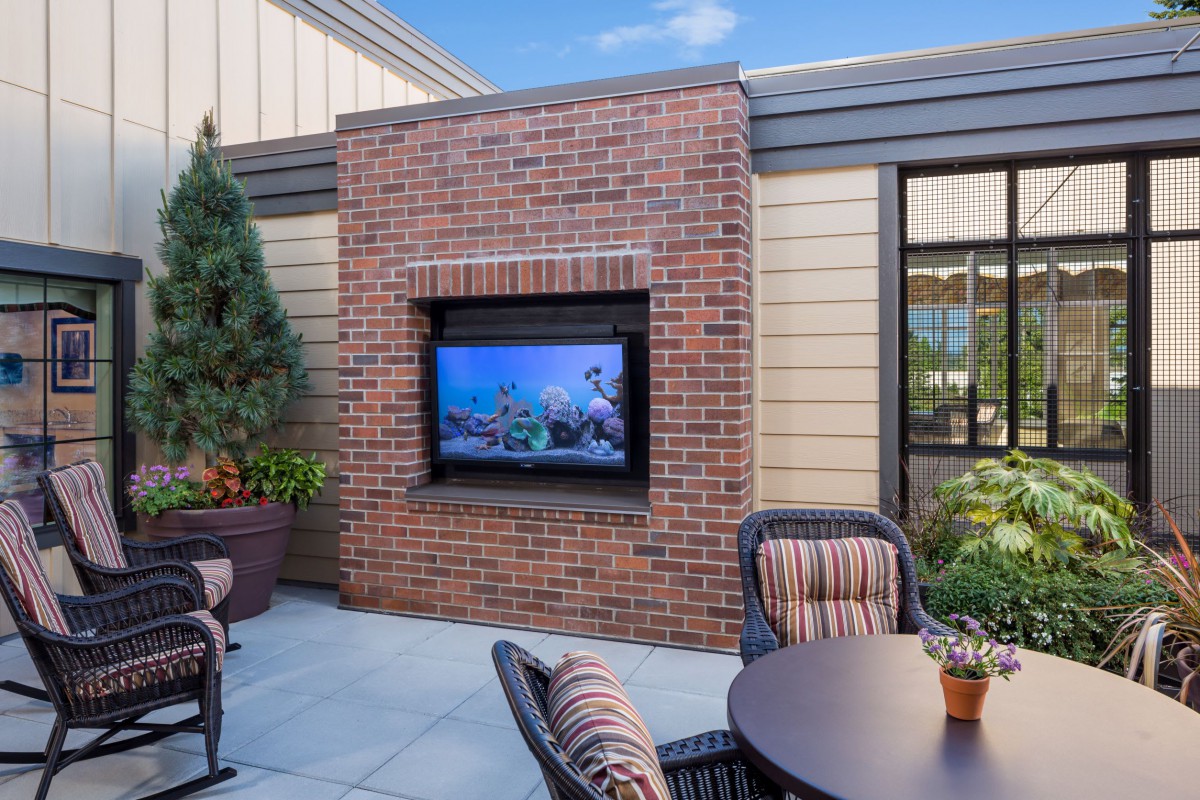 A modern outdoor patio with a brick wall featuring a mounted television, surrounded by comfortable furniture and plants.