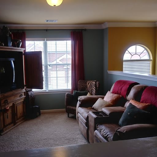 A cozy living room with a sofa, television, and large windows.