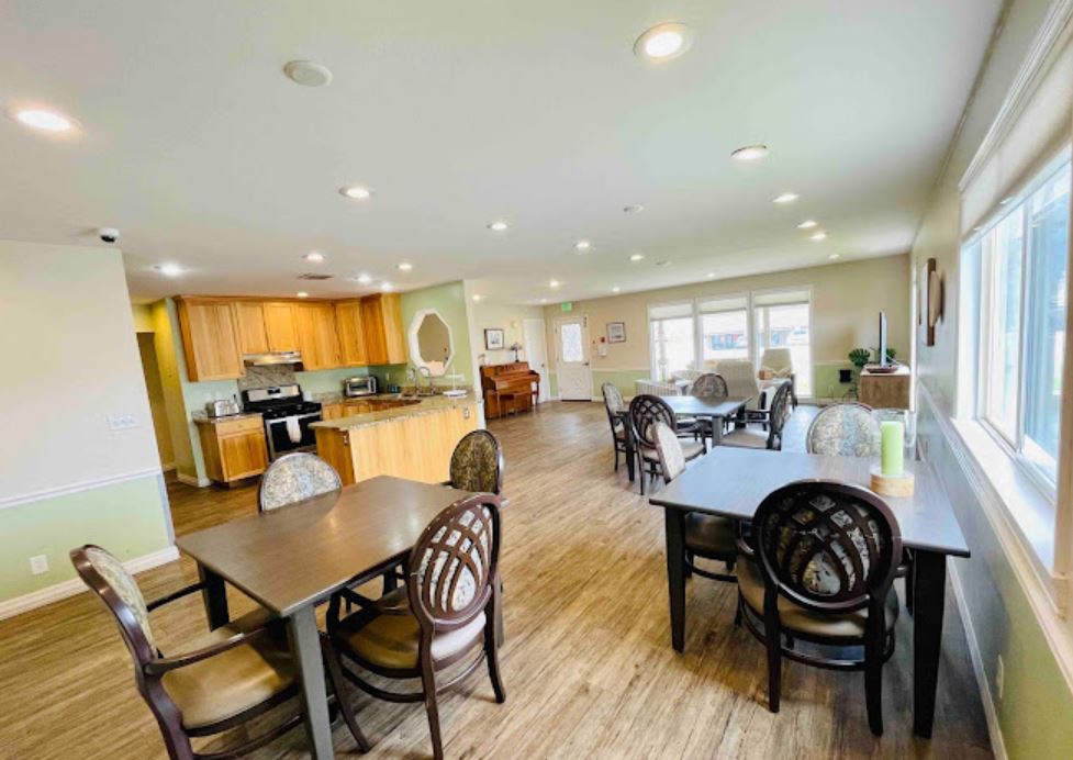 A spacious dining and kitchen area with multiple tables and chairs, illuminated by natural light.