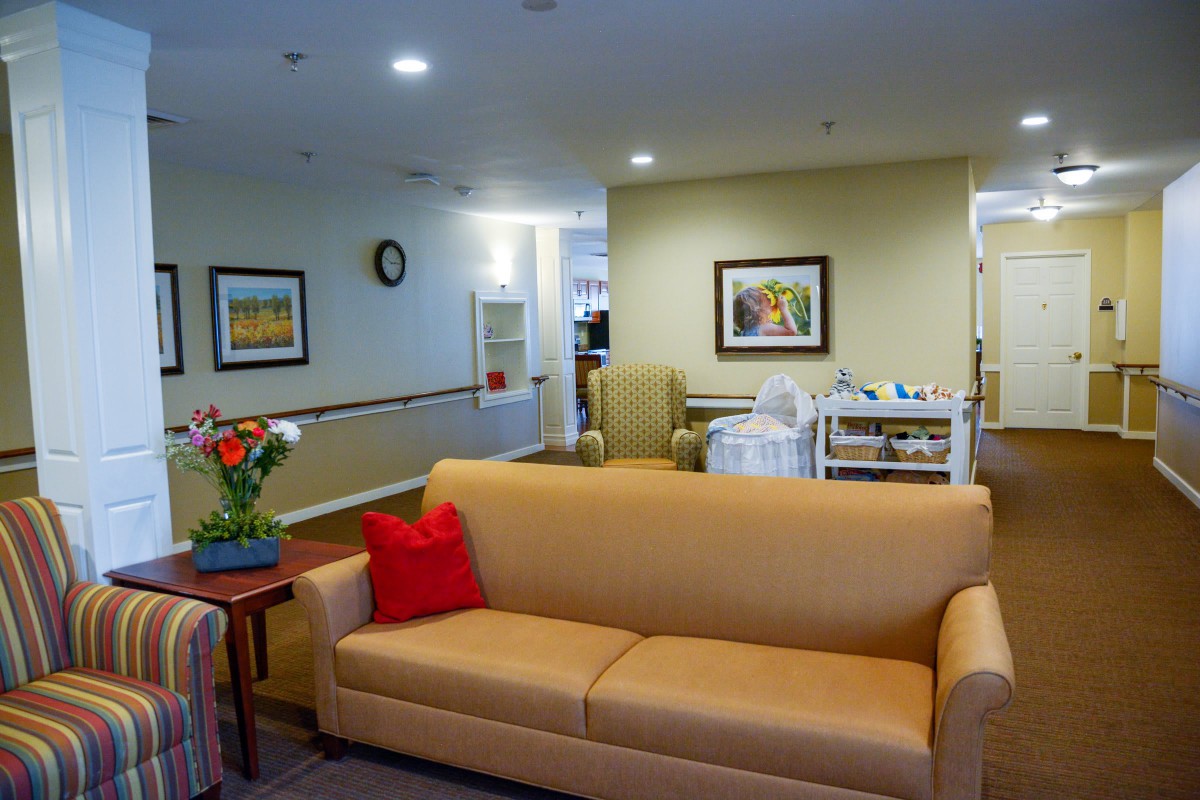 A cozy living room with a yellow couch, colorful pillows, and decorative elements including flowers and artwork.