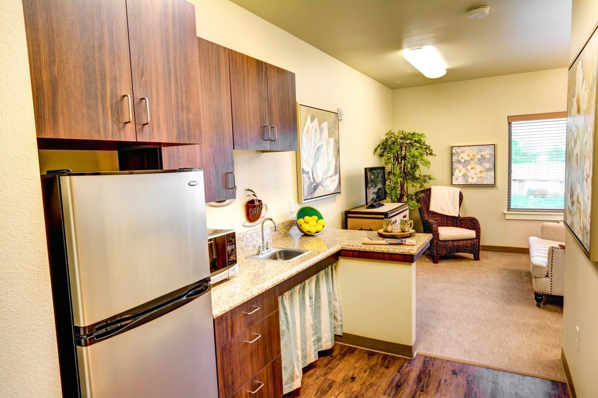 A compact and modern kitchen area in an apartment, featuring wooden cabinets, a stainless steel fridge, and seating.