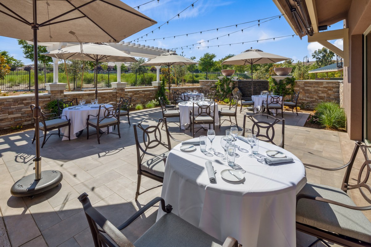 An elegant outdoor dining area with tables set under large umbrellas and decorative string lights, perfect for a sunny day.