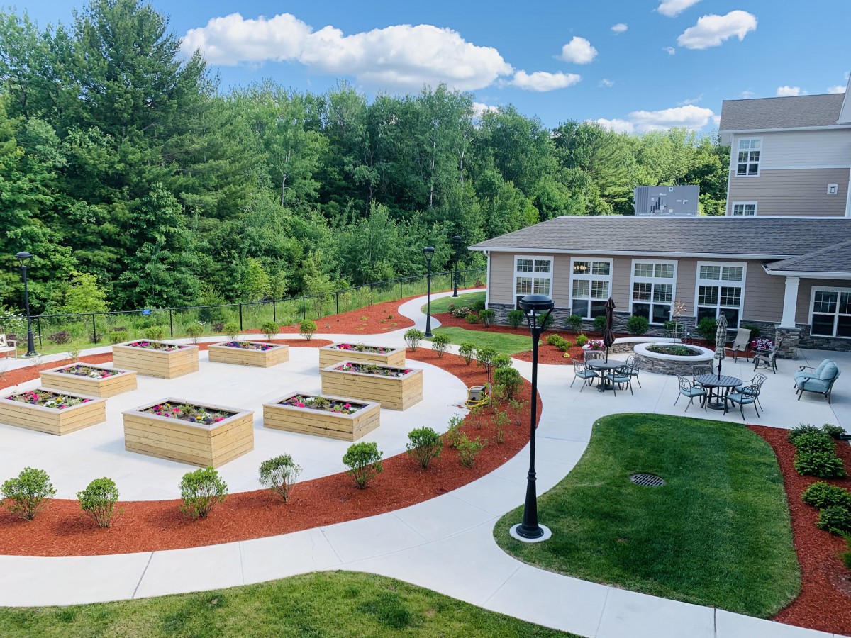 A beautifully landscaped outdoor area featuring raised garden beds, a building, and winding walkways surrounded by lush greenery.