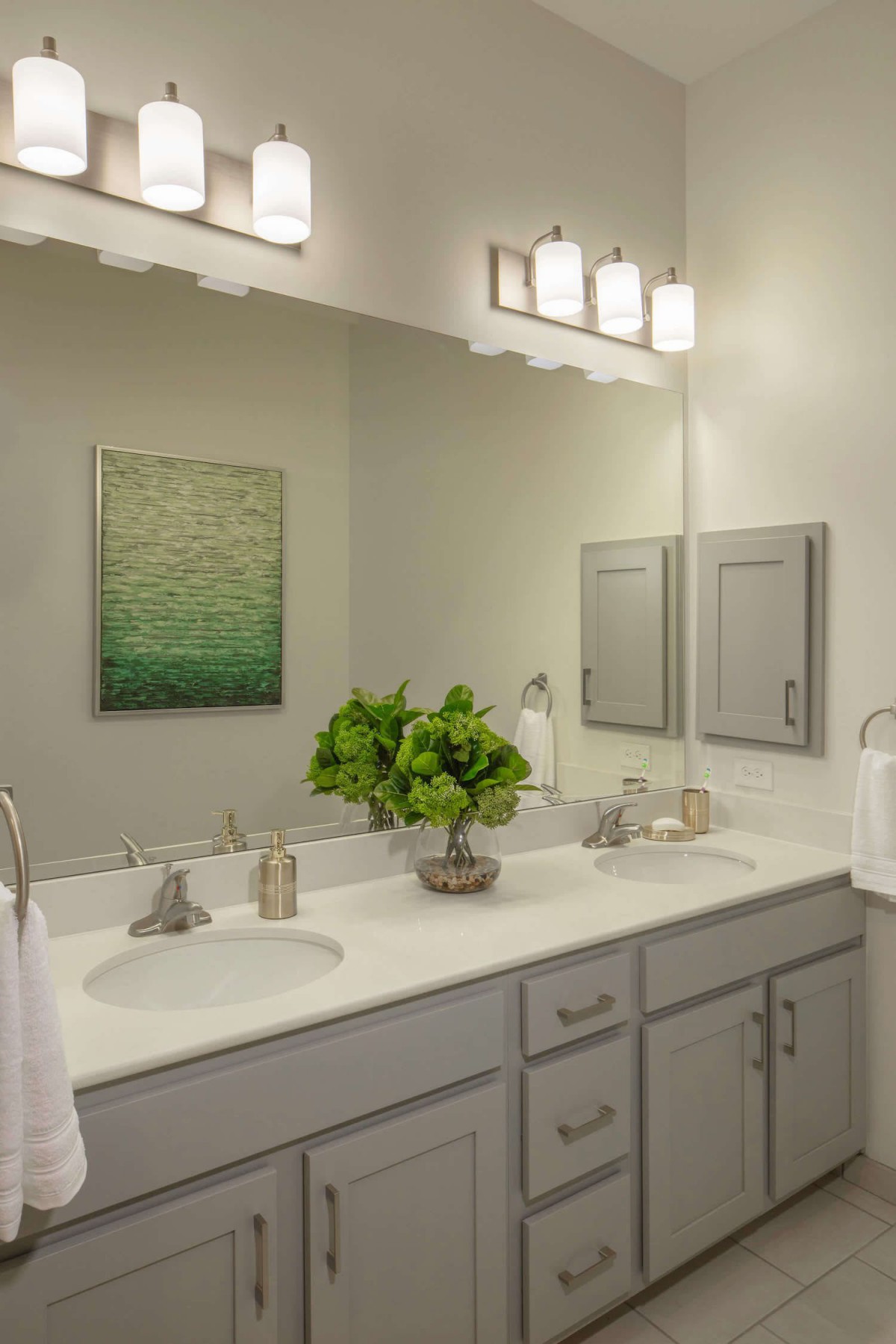 A well-lit bathroom with a double sink vanity and decorative greenery.