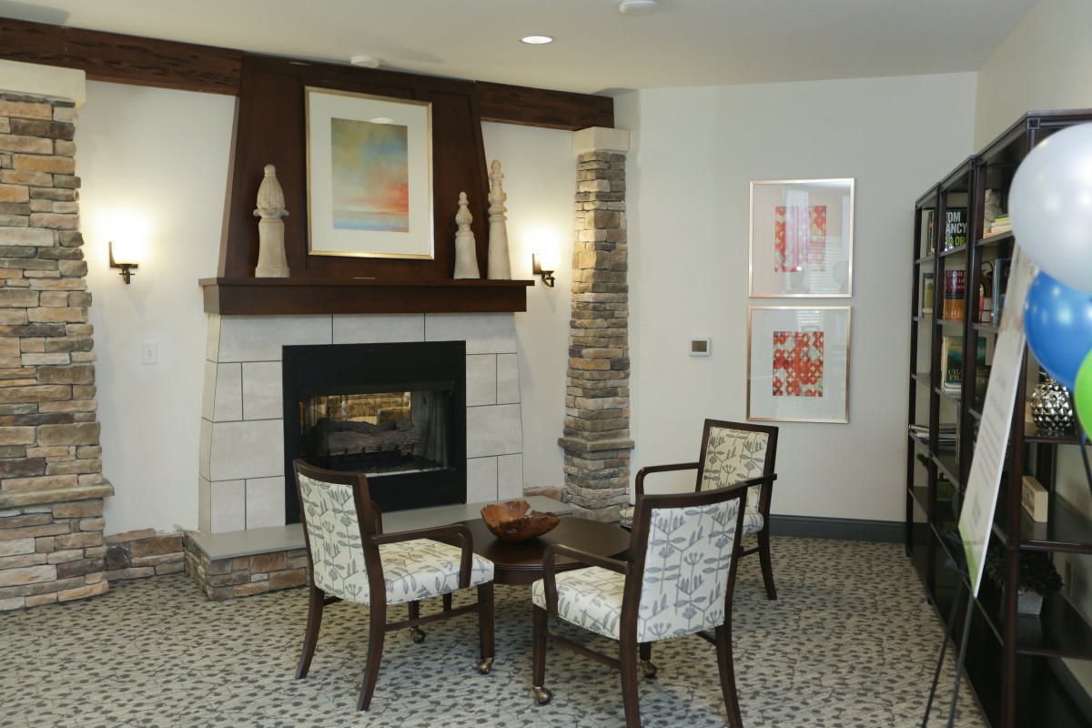 A cozy living room setting with a fireplace, chairs, and artwork on the walls.