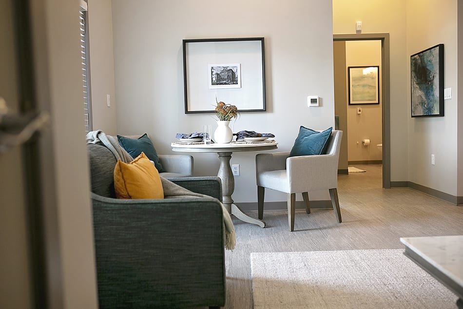 A cozy living and dining space featuring a round table with chairs and a comfortable armchair, accented by colorful cushions and wall art.