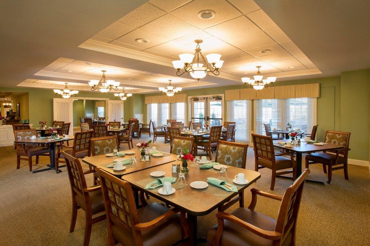 A well-lit dining room with neatly arranged tables and chairs, featuring elegant chandeliers.