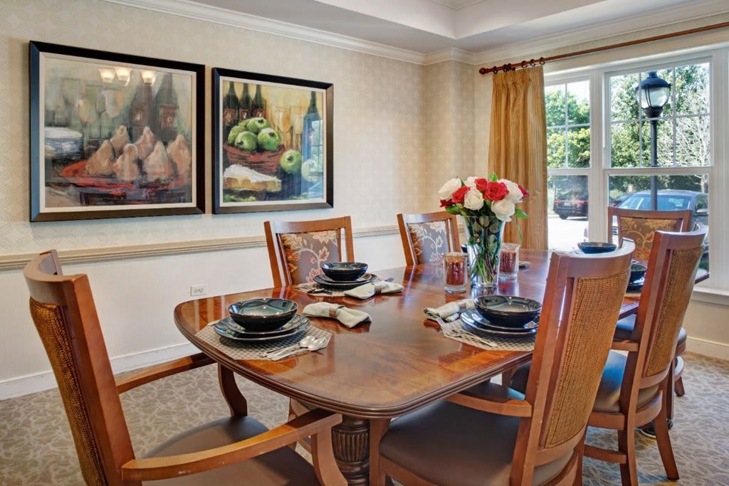 A neatly set dining table in a well-decorated dining room, featuring wooden chairs, elegant place settings, and a vase with flowers.