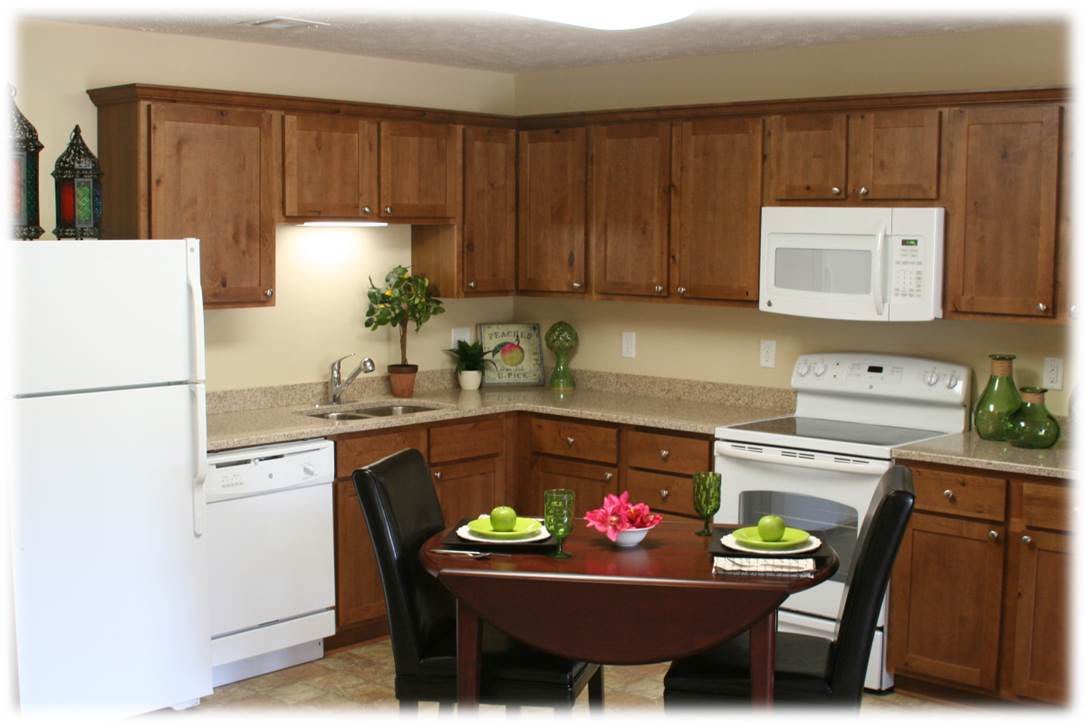 A cozy kitchen with wooden cabinets featuring a small dining table set for two, and equipped with modern appliances.