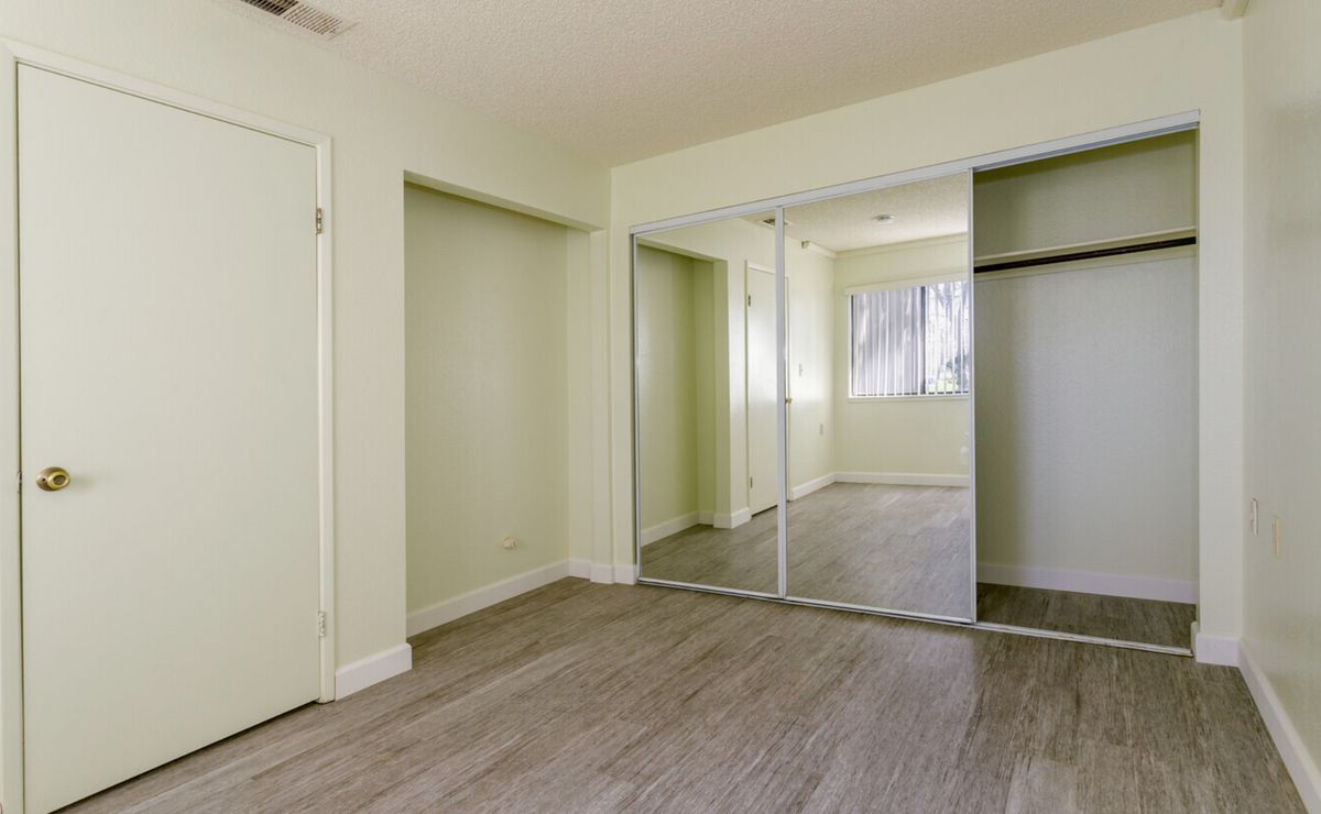 An empty room featuring wooden floors, light green walls, and mirrored closet doors.