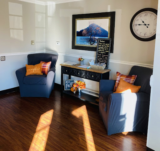 A cozy living room setup featuring two blue chairs with decorative pillows, complemented by a stylish clock and artwork on the wall.