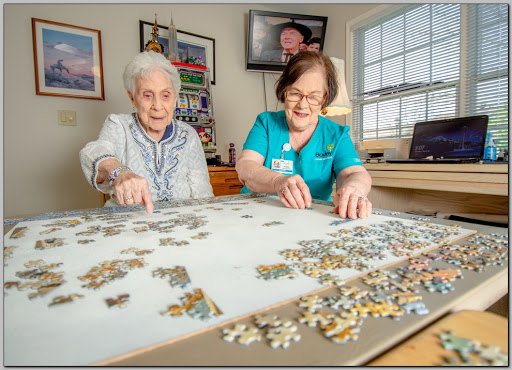 A caregiver and an elderly woman enjoy a fun puzzle activity together, fostering social interaction in a bright and welcoming indoor space.