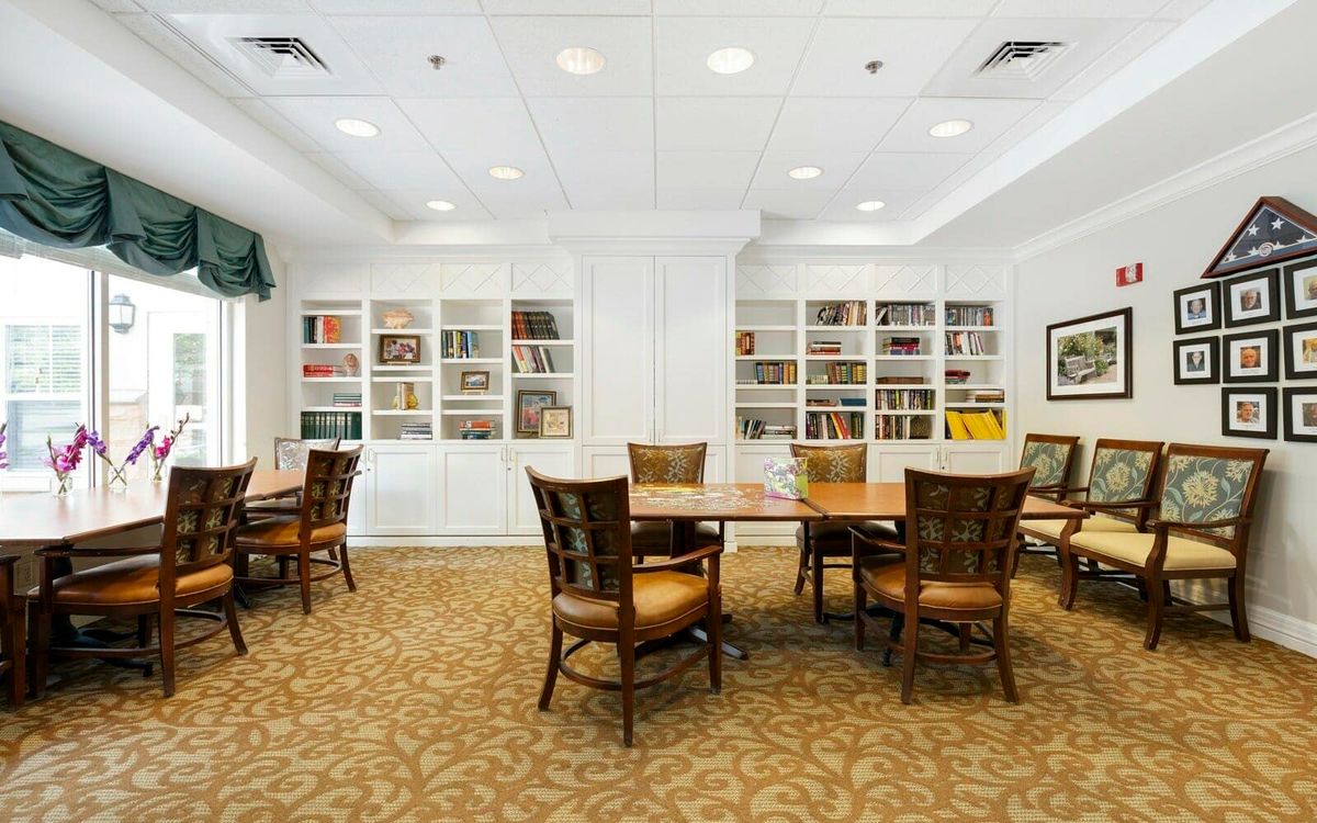 A well-lit library room with bookshelves, tables, and chairs for reading.