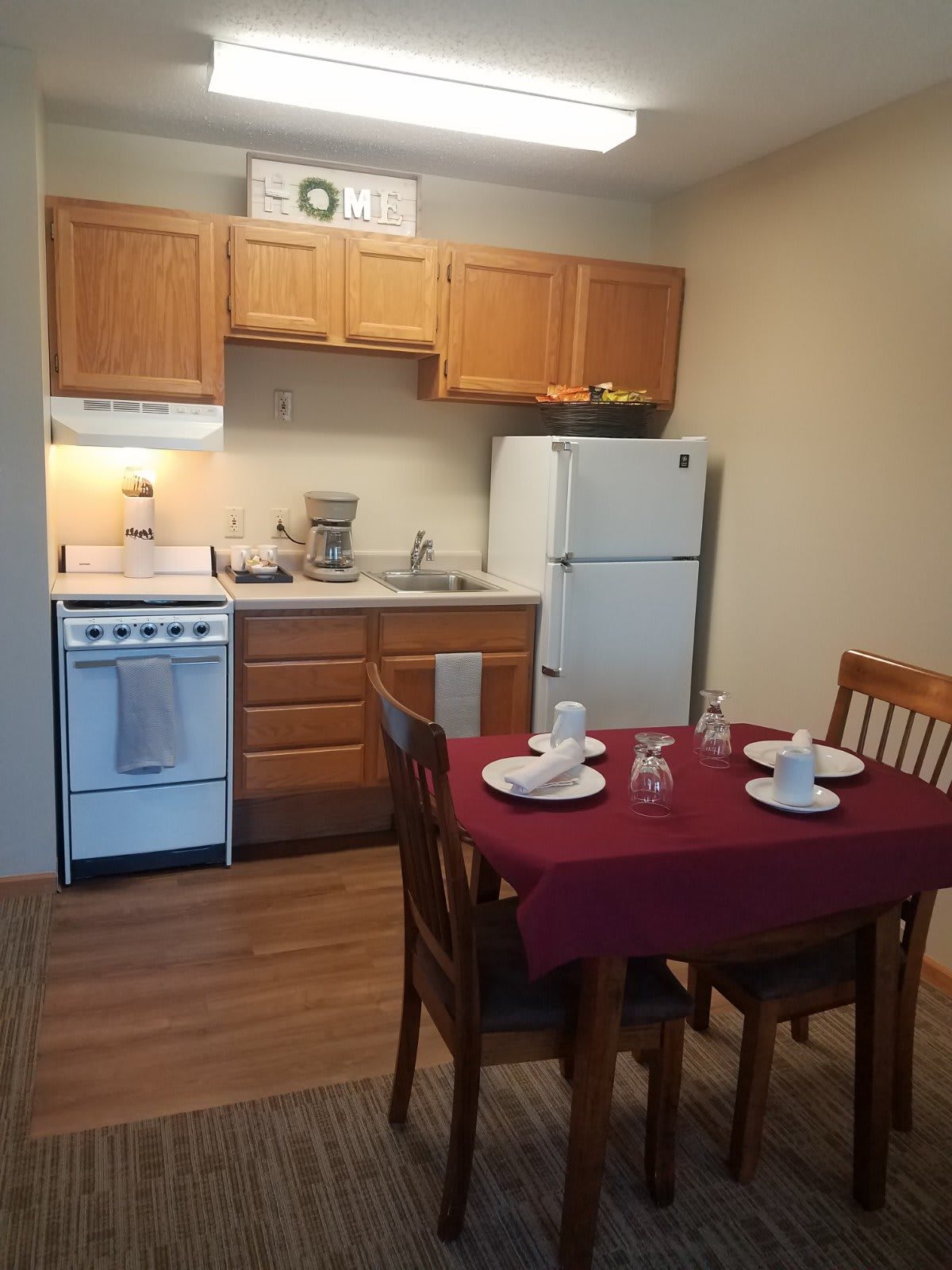 A cozy kitchen and dining area featuring a small table set for four, equipped with a stove, refrigerator, and wooden cabinets.