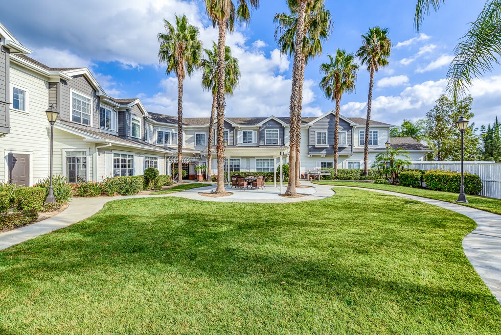 A residential building surrounded by lush green grass and tall palm trees under a blue sky.