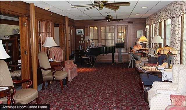 A cozy living room with wood paneling, featuring a piano, various seating options, and warm lighting.
