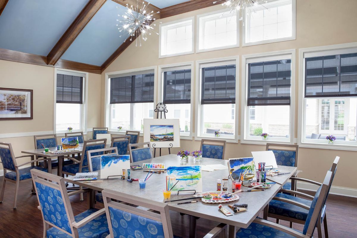 A modern dining room with blue chairs and a set table, illuminated by natural light from large windows.